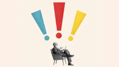 A man in a suit sits in a chair with three large colorful exclamation marks above him.