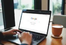 Close-up of hands typing on a laptop displaying the Google search engine on screen