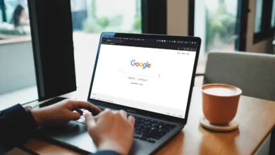 Close-up of hands typing on a laptop displaying the Google search engine on screen