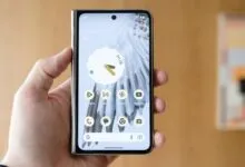 A person holding the Google Pixel Fold smartphone displaying the home screen and app icons.