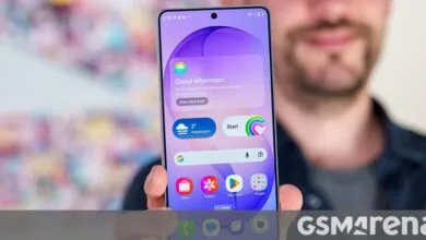 A person holds up a modern smartphone displaying a colorful purple home screen interface.