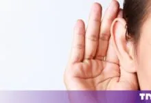 Close-up of a person cupping their hand behind their ear to listen carefully against a plain background