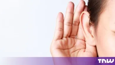 Close-up of a person cupping their hand behind their ear to listen carefully against a plain background
