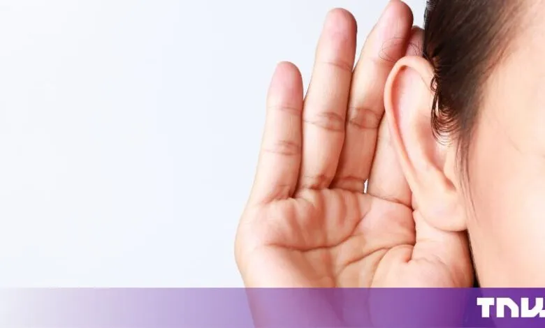 Close-up of a person cupping their hand behind their ear to listen carefully against a plain background