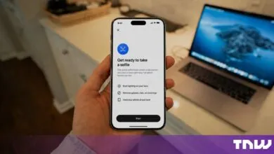 Hand holding a smartphone displaying a selfie verification screen with instructions.