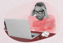Stressed woman with glasses clutching her head while working on a laptop at a desk.