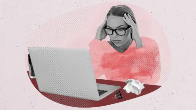 Stressed woman with glasses clutching her head while working on a laptop at a desk.