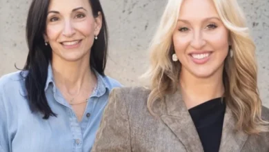 Two women, one with dark hair in a denim shirt and one blonde in a blazer, smiling outdoors.