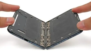 Two hands carefully pull apart the internal hinge mechanism of a disassembled foldable smartphone.