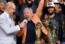 James Dolan celebrates with Ernie Johnson Jr. and NBA championship trophies after a victory.