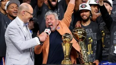 James Dolan celebrates with Ernie Johnson Jr. and NBA championship trophies after a victory.