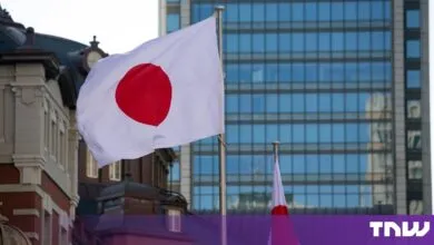 Japanese flag waving in the wind against a backdrop of modern and historic city buildings.