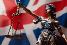 Statue of Lady Justice holding scales against a blurred UK flag background