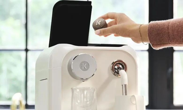 A person placing a K-Cup pod into a modern white Keurig coffee machine