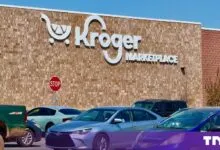 Exterior facade of a Kroger Marketplace store with a large brick wall and parking lot full of cars.