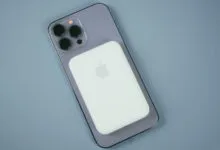 Purple iPhone with triple camera array attached to a white MagSafe battery pack on a blue surface.