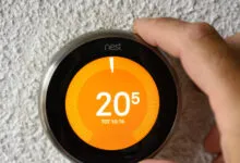 A person adjusting the temperature on a round digital Google Nest thermostat mounted on a textured white wall.