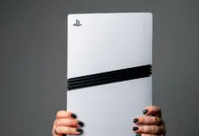 A pair of hands with dark nail polish holds a white PlayStation 5 console upright.