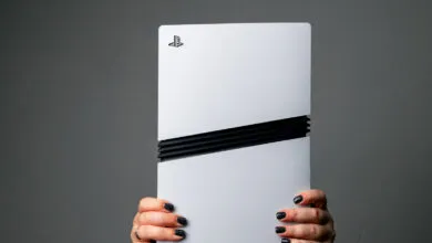A pair of hands with dark nail polish holds a white PlayStation 5 console upright.