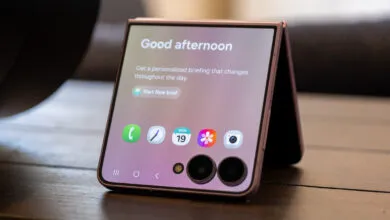 Pink foldable smartphone standing on a table in flex mode displaying app icons and a welcome message