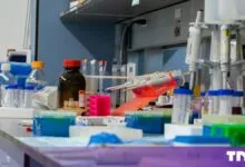 A cluttered laboratory bench with various scientific equipment, test tubes, pipettes, and reagent bottles.