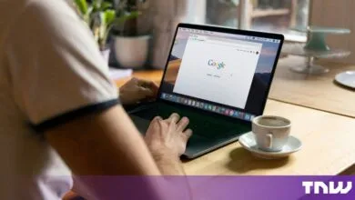 Person using a laptop with the Google search engine open on a wooden table beside a coffee cup.