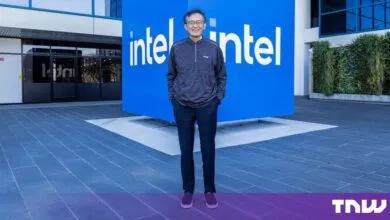 Lip-Bu Tan stands smiling in front of a large blue Intel logo cube at the company's headquarters.