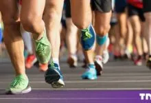 Close-up of diverse marathon runners' legs and colorful running shoes sprinting on a city road.