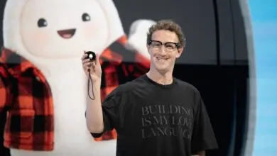 Meta CEO Mark Zuckerberg holding up a small black device on stage in front of a cartoon mascot