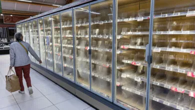 A woman walks past empty grocery store refrigerators following a cyberattack.