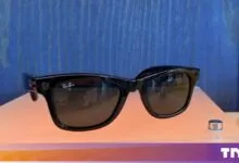 Black Meta Ray-Ban smart glasses displayed on an orange surface against a blue wooden background.