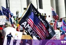 A protester holds a black flag reading 'No Kings in America' with a stylized US flag design at a rally.