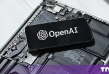 Smartphone displaying the OpenAI logo resting on open laptop hardware components.