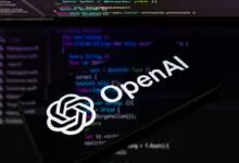 OpenAI logo displayed on a smartphone screen against a dark background of programming code
