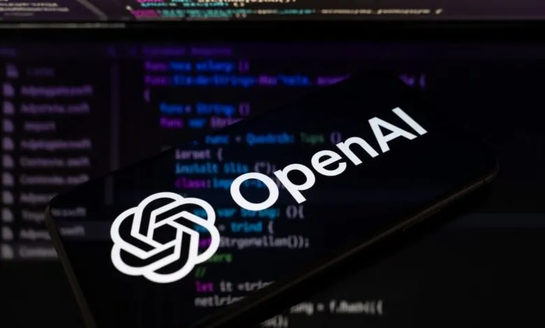 OpenAI logo displayed on a smartphone screen against a dark background of programming code