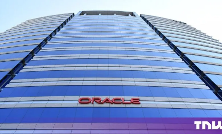 Low-angle view of the Oracle building facade featuring blue glass and red signage against the sky.