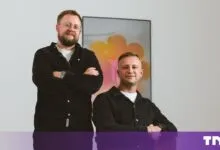 Two Pandektes co-founders pose together in a bright studio with a colorful modern art piece behind them.