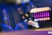 Close-up of a photon bridge laser chip glowing with vibrant purple light and connected fiber optics.