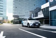 A white Pony.ai autonomous robotaxi driving on a city street flanked by modern skyscrapers.