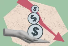 A grayscale hand supports three dollar sign coins beneath a downward trending red arrow.