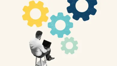 Man sitting on a stool working on a laptop beneath colorful gear graphics