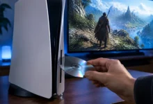 A person inserting a disc into a PlayStation 5 console while a fantasy game plays on the TV