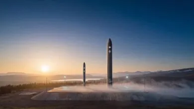 Two sleek black rockets stand upright on a concrete launchpad during sunrise over a mountainous landscape.
