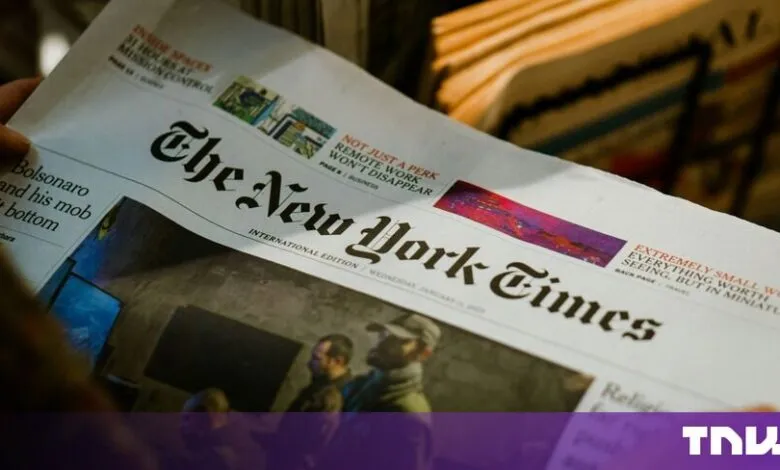 Close-up of a person holding the front page of The New York Times International Edition newspaper.