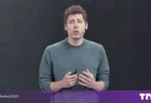 Sam Altman wearing a green sweater speaks on a dark stage during OpenAI DevDay.