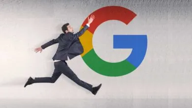 A businessman in a suit runs towards a large colorful Google logo on a textured wall.