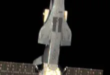 A futuristic military space plane with solar panels in deep space against a dark background.