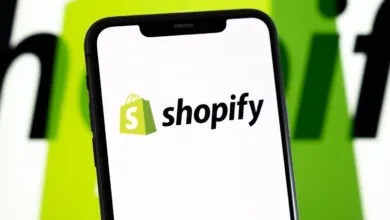 Smartphone displaying the Shopify logo on its screen against a blurred green and white background.