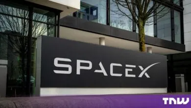 A black SpaceX logo sign standing outside a modern office building with glass windows.