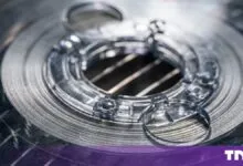 Close-up view of a metallic spool of superconducting tape with a complex center hub.